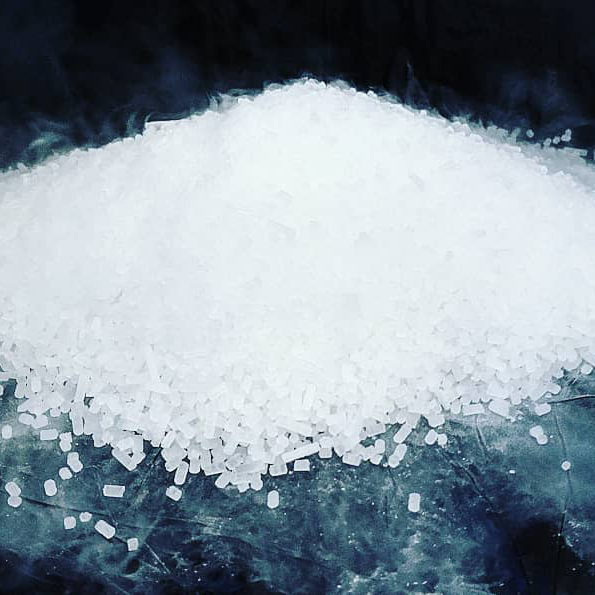 Haufen weißer Trockeneispellets auf dunkler Oberfläche mit aufsteigendem Nebel.