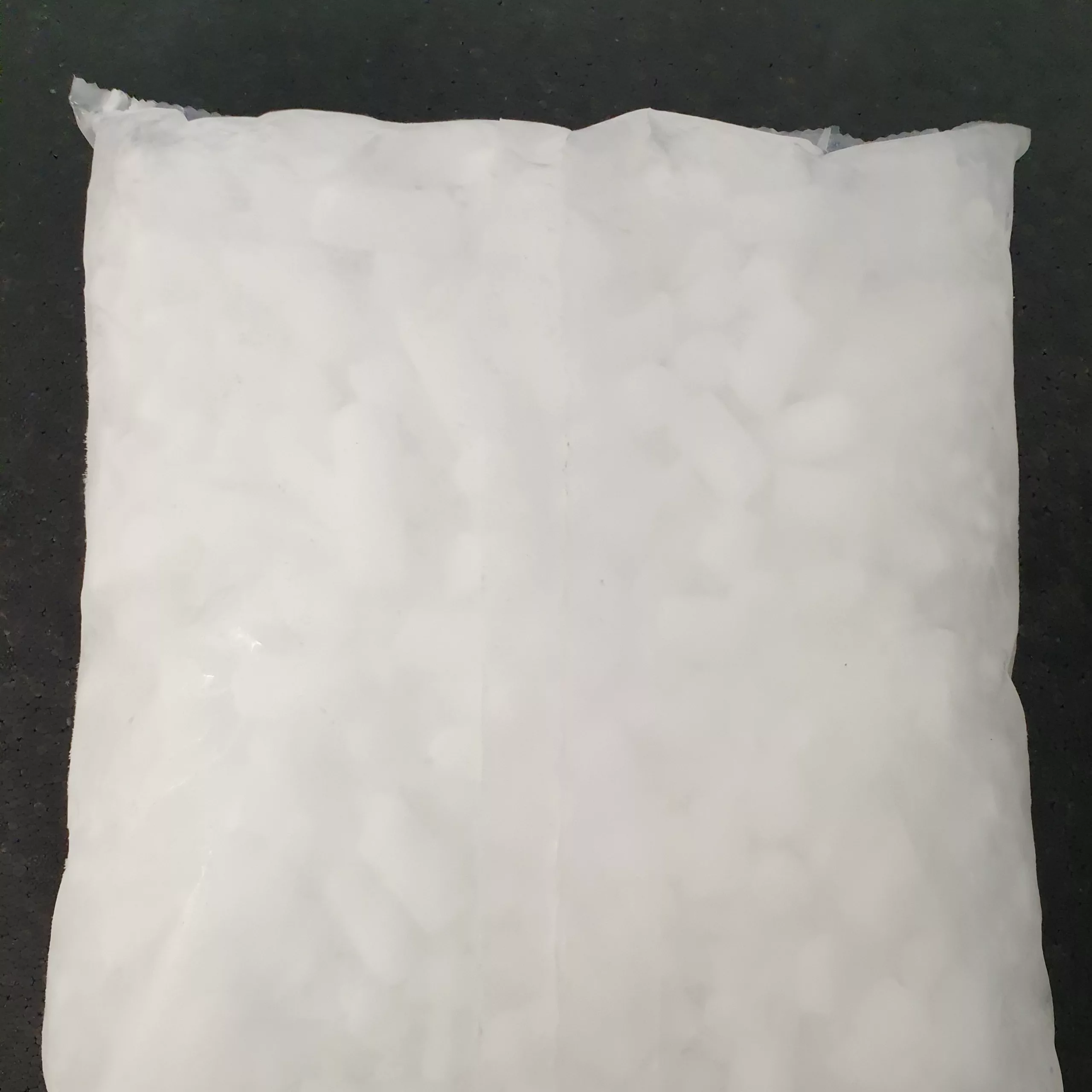 Weißer, rechteckiger Beutel mit Trockeneis, auf dunklem Untergrund liegend.