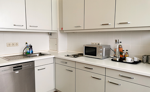 Kleine weiße Küche mit Spüle, Geschirrspüler, Mikrowelle und Tassen auf der Arbeitsplatte.