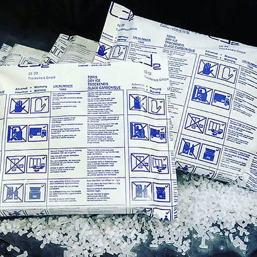 Mehrere weiße Verpackungen mit blauen Piktogrammen und Warnhinweisen liegen auf einer Schicht aus kleinen weißen Trockeneiskügelchen.