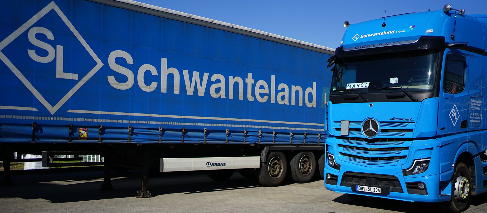 Blauer Lkw mit Mercedes-Stern und Aufschrift 'Schwanteland' auf dem Anhänger, geparkt auf Asphalt.