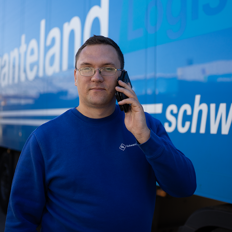 Mann in blauem Sweatshirt mit weißem Logo telefoniert vor blauem Lkw mit weißer Schrift.