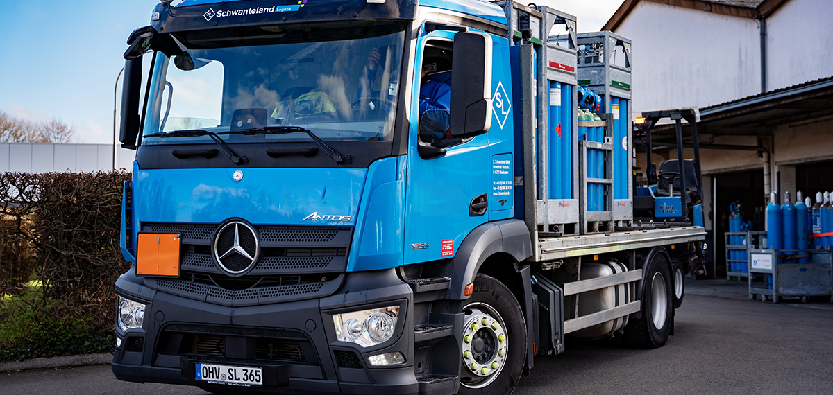 Blauer Mercedes-Lastwagen mit Aufschrift 'Schwanteland Logistik' transportiert mehrere Gasflaschen in Metallgestellen.