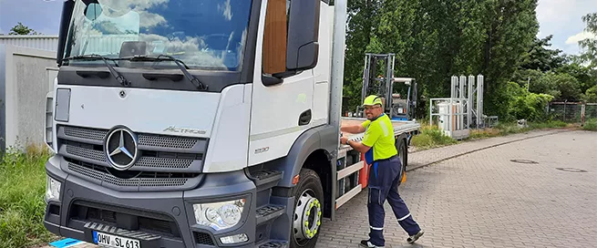 Weißer Mercedes-Actros-Lkw mit Fahrer in gelbem T-Shirt und blauer Hose, der an der Fahrerseite steht.
