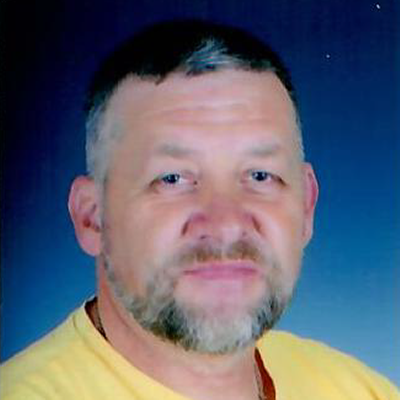 Oberkörper eines Mannes mit kurzem Haar, gelbem T-Shirt vor blauem Hintergrund.