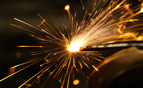 technische_gase_schneidgase2_schwanteland Funkenflug beim Schneiden oder Schweißen mit technischem Gas, helle Lichtquelle mit strahlenförmigen Funken auf dunklem Hintergrund.