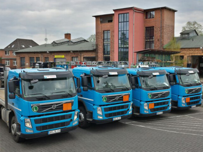35_jahre_Schwanteland_beitrag_web6 Mehrere blaue Volvo-Lkw stehen nebeneinander auf einem Parkplatz vor einem roten Backsteingebäude